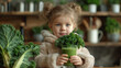 Little toddler girl in a white fluffy jacket holds a bunch of fresh kale and is about to drink a green smoothie in the kitchen. 