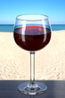Glass of red wine on a wooden table at a beach bar. Picturesque background with sand and sea. Balloon style glass. 3d rendering.