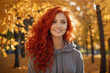 A beautiful girl with red hair in a sunny autumn park. Yellow maple leaves are falling from the sky.