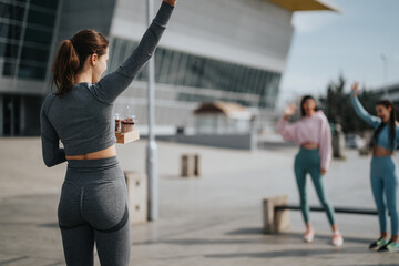 woman in fitness attire greeting friends in urban setting, showcasing active lifestyle and friendshi