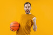 © wpadington - Studio portrait of young attractive basketball player or supporter posing over bright colored orange yellow background holding the ball in hand and making winner's gesture clenching his fist