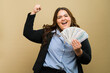 Cheerful plus-size woman smiling and holding cash, celebrating her monetary achievement in a studio setting