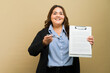 Portrait of a cheerful plus-size woman requesting signature on a contract with a pen in a studio setting