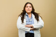 Confident plus-size doctor in lab coat poses with crossed arms in a studio setting