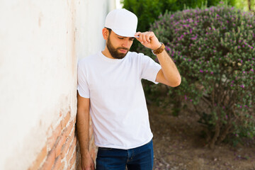 Wall Mural - Bearded young hispanic man wearing a blank white t-shirt and cap, ideal for brand mockup designs, standing outdoors