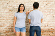 Smiling hispanic couple in plain gray t-shirts posing for branding against a weathered brick wall background