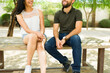 Closeup of a young couple sitting on a bench outdoors, smiling and chatting on a sunny day, exuding casual latin romance vibes
