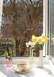 Cup of tea,croissant and spring flowers in a vase on a sunny window.The concept of home comfort and greeting of spring.Beautiful flower arrangement with hyacinths and daffodils,selective focus.