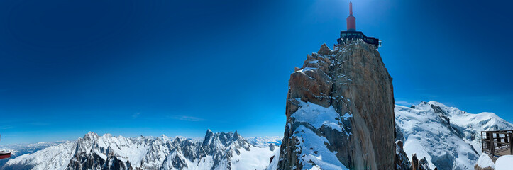 Haute-Savoie, France, 04-25-2024: blue sky and panoramic view of L’Aiguille du Midi (Needle at midday), the highest spire (3.842 m) of the Aiguilles de Chamonix, with the Mont Blanc massif peaks 