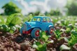 A blue toy truck is on a field of soil with small green plants growing around it.