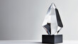 A crystal trophy with geometric facets on a black pedestal against a gray background.