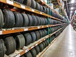 Displayed within a warehouse at a tire store, rows of car tires and wheels await their destined vehicles. The neatly organized arrangement highlights the variety