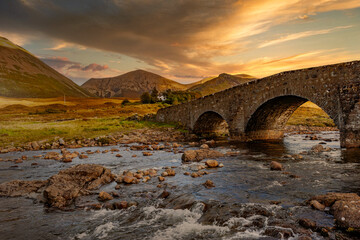 Wall Mural - Sligachan Bridge, Isle of Skye, Scotland, with Cuillin Mountains and orange clouds on backround in sunset light, Isle of Skye, Scotland