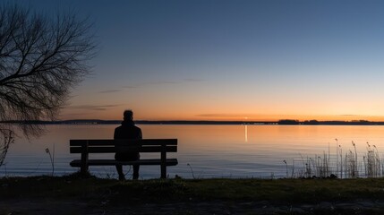 Lonely person sitting on a wooden bench alone at dusk looking at the sunset