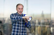 Confident elderly mature man giving a speech in megaphone and pointing at something. Boss giving a command. Blurred indoors background.