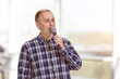 Portrait of a handsome mature man is singing standing indoors. Bright blurred background.