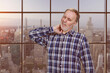 Handsome mature caucasian man is having a neckache. Checkered windows background with cityscape view.