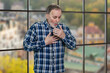 Portrait of a mature man coughing standing indoors. Windows background with cityscape view.