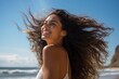 A Latina Brazilian woman standing with her hair gathered by the seaside laughing summer smile.