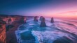 The image shows a beautiful sunset over the Twelve Apostles, a series of limestone stacks off the coast of Victoria, Australia. The sky is a vibrant mix of oranges, pinks, and purples, and the water i