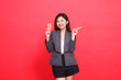 Cheerful indonesia office woman's expression holding a debit credit card while pointing to the left wearing a jacket and skirt on a red background. for financial, business and advertising concepts
