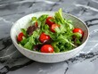 A high-angle view of a simple salad in a white ceramic bowl, with fresh greens and cherry tomatoes.
