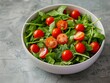 A high-angle view of a simple salad in a white ceramic bowl, with fresh greens and cherry tomatoes.