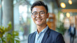 © boxstock production - Happy young Asian businessman in stylish clothes and glasses smiling friendly against blurred modern office room background