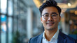 © boxstock production - Happy young Asian businessman in stylish clothes and glasses smiling friendly against blurred modern office room background
