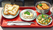 cafeteria tray holding a plate of 2 toasted sliced breads with butter sits on it and a bowl of Japanese katsu-don and a plate of potato salad 