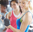 Woman, dumbbell and gym exercise or weightlifting workout for bicep growth or muscle, arms or strong. Female person, friends and fitness training for wellness goals in group class, health or smile