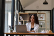 © Wasana - Smiling young businesswoman with curly hair working on her laptop at a well-organized office desk.