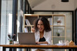© Wasana - Ecstatic businesswoman with curly hair cheering at her desk after receiving positive news on her laptop in the office.