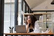 © Wasana - Joyful businesswoman with curly hair celebrating a successful moment while working at her modern office desk.
