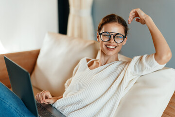 Wall Mural - Happy woman working on a laptop in her cozy home office, surrounded by modern interior and technology With a smile on her face, she enjoys the comfort of the couch while confidently typing away on her