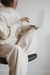 Pretty woman in white clothes using laptop computer over white wall. Web, internet, social media online surfing. Neutral beige color