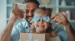 © Алексей Василюк - A happy father holds his daughter in one hand and an open gift box with a blue ribbon wrapped around it, which contains postcards with heart-shaped stickers on them, covering her eyes to surprise her