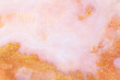 White and pink acrylic paints with shimmering golden glitter. Colorful liquid paint abstract background.
