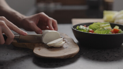 Wall Mural - man hands slicing mozzarella on wood board on home kitchen