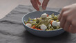 man hand add mozzarella balls to green fettuccine with pesto in blue bowl