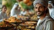 A smiling man in traditional Middle Eastern attire posing in front of a buffet of regional dishes. 