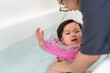 Asian little baby girl swimming and wear rubber ring on neck in bathtub, Mother holding daughter for safety support, Living lifestyle family indoors concept.