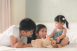 lder asian sister and Elder asian brother playing animal hand puppet doll toys with younger asian sister, sitting on bed, Educational preschool games, Having fun with kid at home concept.