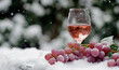 Glass of rose wine on snow in winter and ripe bunch of grapes