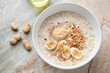 Oatmeal with peanut butter, banana and granola in a white bowl, horizontal shot on a grey and roseate granite background, elevated view