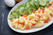 Scrambled eggs with smoked salmon and cucumber salad on a white plate, horizontal shot on a black marble background, middle closeup