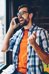 Wall Mural - Happy young man talking on smartphone and rejoicing of victory of successful project.Excited hipster guy celebrating win calling on cellular.Amazed blogger received good news during phone conversation