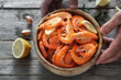 Male hands holding a wooden bowl with fresh fried shrimp on a wood background top view