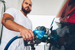 © BullRun - Serious bearded hipster guy filling talk of automobile for driving holding hose and nozzle on service station,young male owner of car refill vehicle with petroleum, climate pollution concept