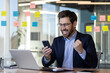 © Liubomir - Mature boss businessman celebrating victory success, man at workplace with phone in hands, got good news online in email, boss educated worker in business suit holding hand up triumph gesture.